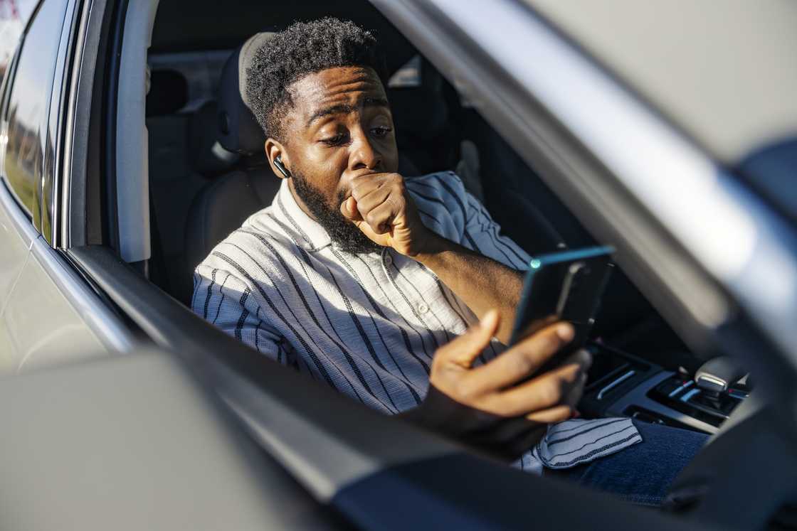 A man in car is reading excited news on cellphone.
