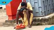 Tired hawker girl resting by road with scanty tomatoes on her plate and cross around her neck makes many sad